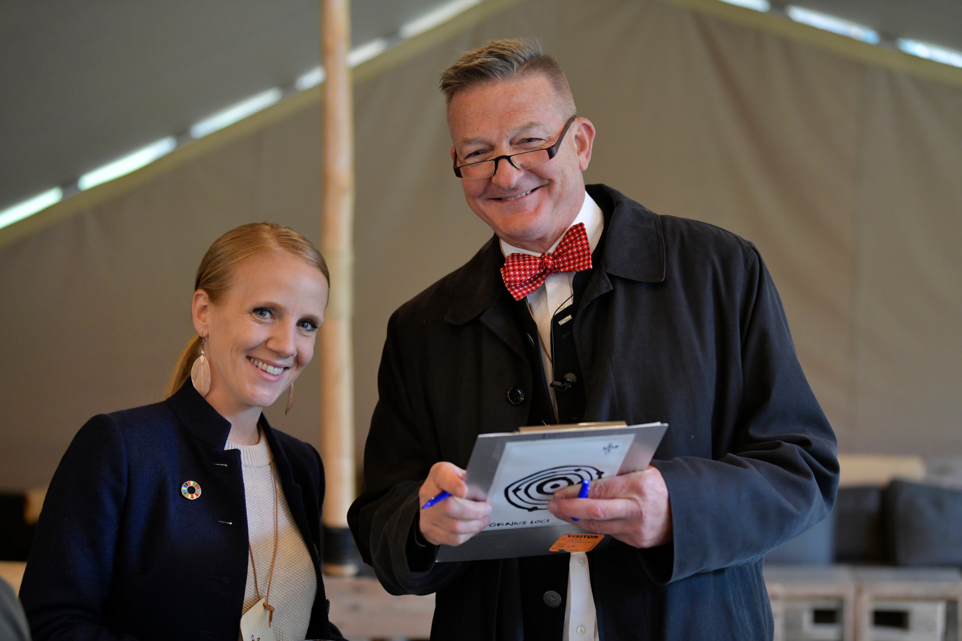 Two people smiling together at a workshop, one holding a clipboard